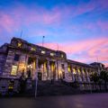 The exterior of the New Zealand Parliament building at 1 Museum Street, Pipitea in Wellington at sunset with pink-coloured clouds in the sky above.