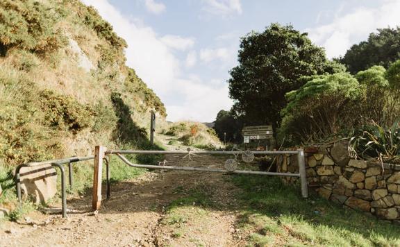 The entry to Tip Track on Happy Valley Road. There is a locked gate with metal art on it, including a biker, dog, and walker. Behind it there is a sign showing you are on Tip Track.