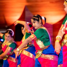 Four Indian women dressed in traditional garb performing a dance.