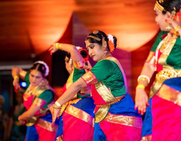 Four Indian women dressed in traditional garb performing a dance.