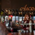 A bartender at Ascot pours a sangio. Large mirrors on the wall behind them reflect outside, and the sign hangs above their head.