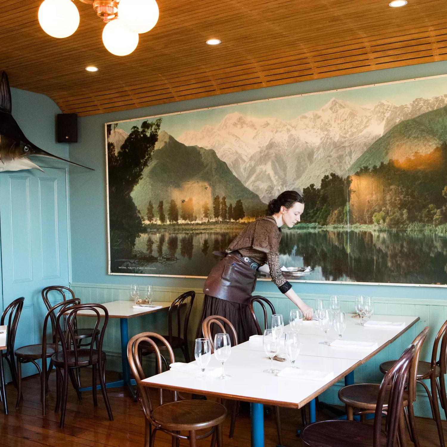 Waiter setting a table inside Ortega Fish Shack. A large Marlin is mounted on one wall and a very large painting of a lake is on the other.