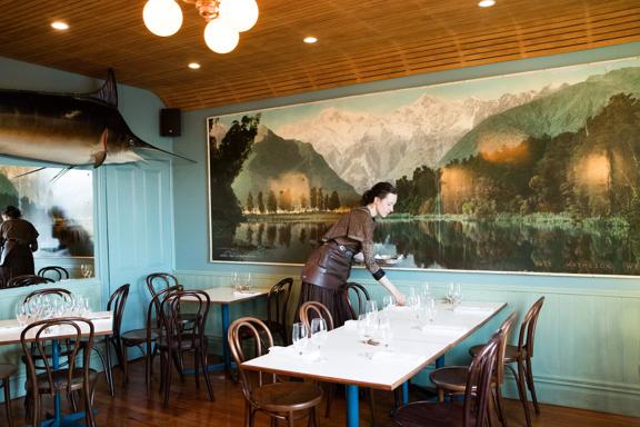 Waiter setting a table inside Ortega Fish Shack. A large Marlin is mounted on one wall and a very large painting of a lake is on the other.