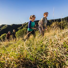 Two people walking up a grassy hill on the Link Track in Whareroa Farm.