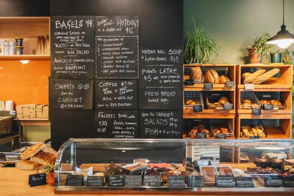 The counter at The Bond Street Deli with plenty of baked goods for sale and a chalkboard menu on the back wall.