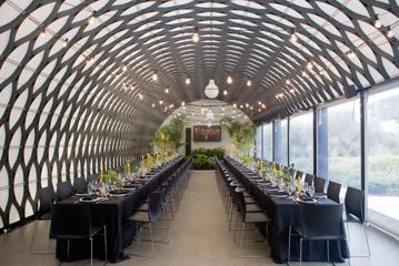 Inside the Kamala function room at Wellington Zoo, the ceiling is an intricate metal mesh, the floors are concrete, and two long tables with black tablecloths and decorations run the room's length with seats on either side.