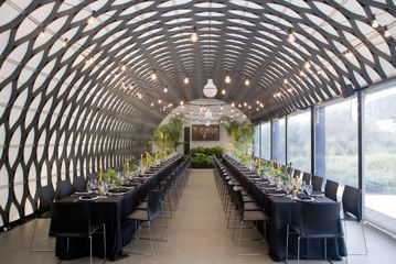 Inside the Kamala function room at Wellington Zoo, the ceiling is an intricate metal mesh, the floors are concrete, and two long tables with black tablecloths and decorations run the room's length with seats on either side.