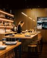 Waiter setting a table at Koji, the room has dim lighting and a large wooden feature wall.