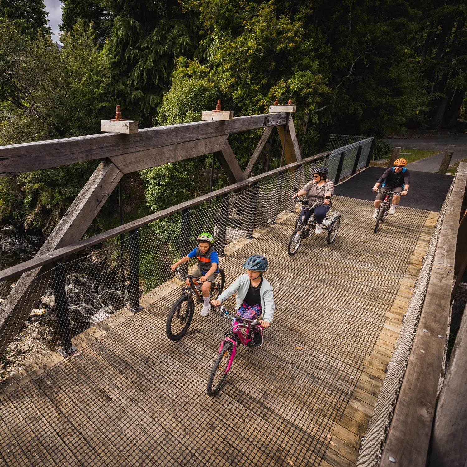 Two adults and two children cycling across a wooden bridge over a river.