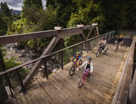 Two adults and two children cycling across a wooden bridge over a river.