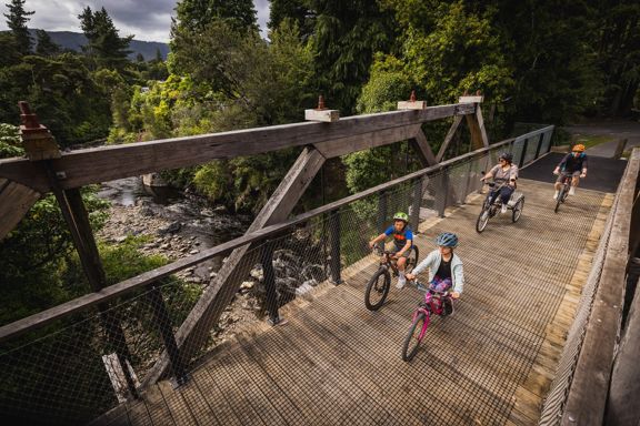Two adults and two children cycling across a wooden bridge over a river.