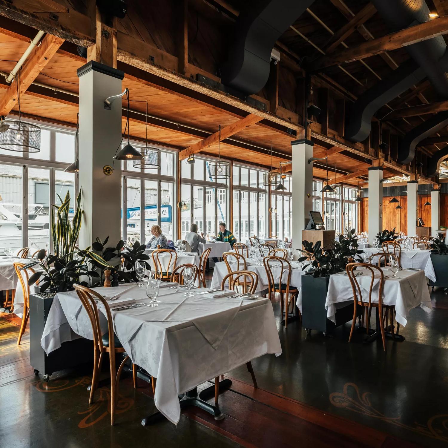 The interior of Shed 5 Restaurant is located on Wellington's waterfront. The large space has high ceilings, exposed beams, dark wood floors and tables set with white tablecloths.
