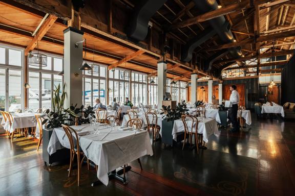 The interior of Shed 5 Restaurant is located on Wellington's waterfront. The large space has high ceilings, exposed beams, dark wood floors and tables set with white tablecloths.