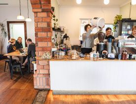 Inside one of Swimsuit's three cafés at 91b Park Road, Miramar. Three staff members are working behind the counter while patrons enjoy coffee.