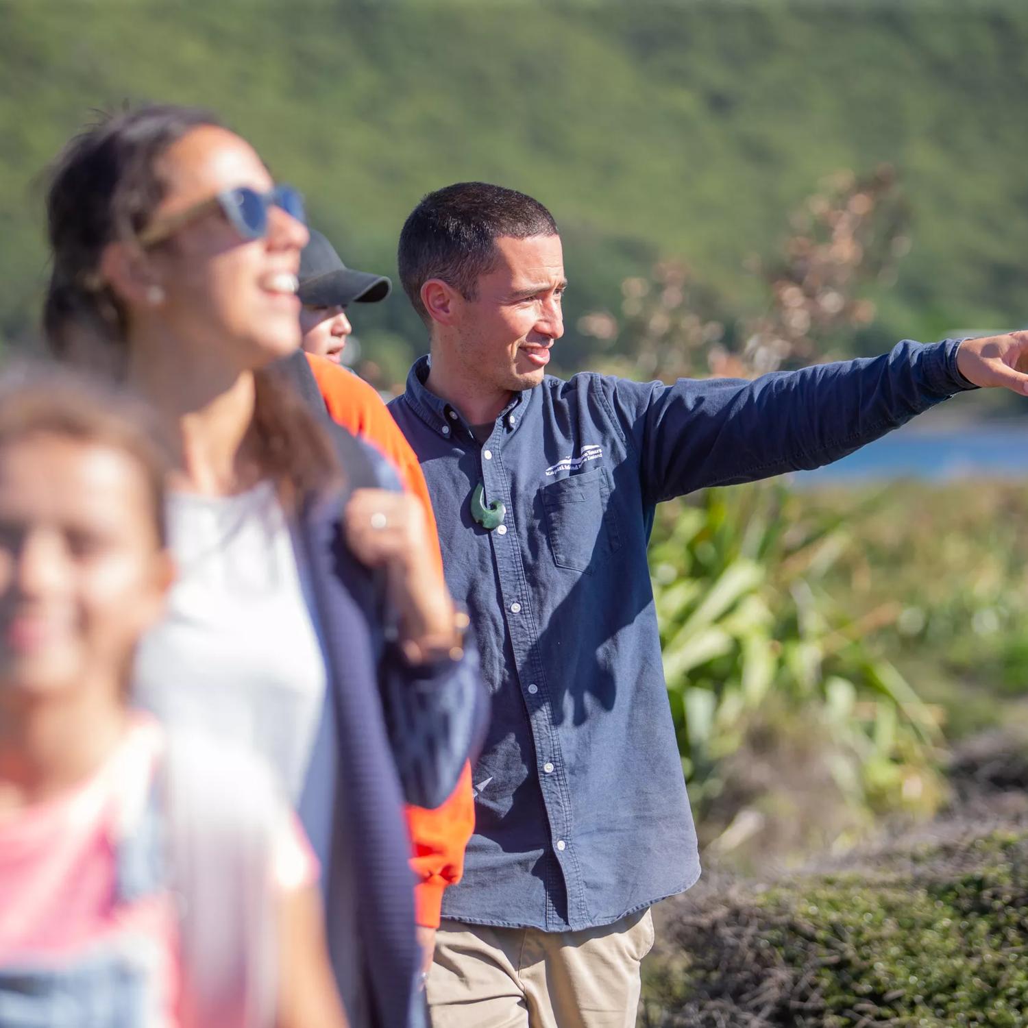 Five people walk one in front of the other along a nature trail. One of them is gesturing with their left arm raised.