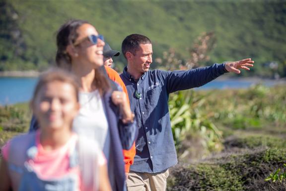 Five people walk one in front of the other along a nature trail. One of them is gesturing with their left arm raised.