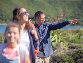 Five people walk one in front of the other along a nature trail. One of them is gesturing with their left arm raised.