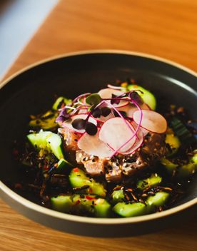 A raw tuna salad dish with smashed cucumbers and crispy rice garnished with radish and microgreens.