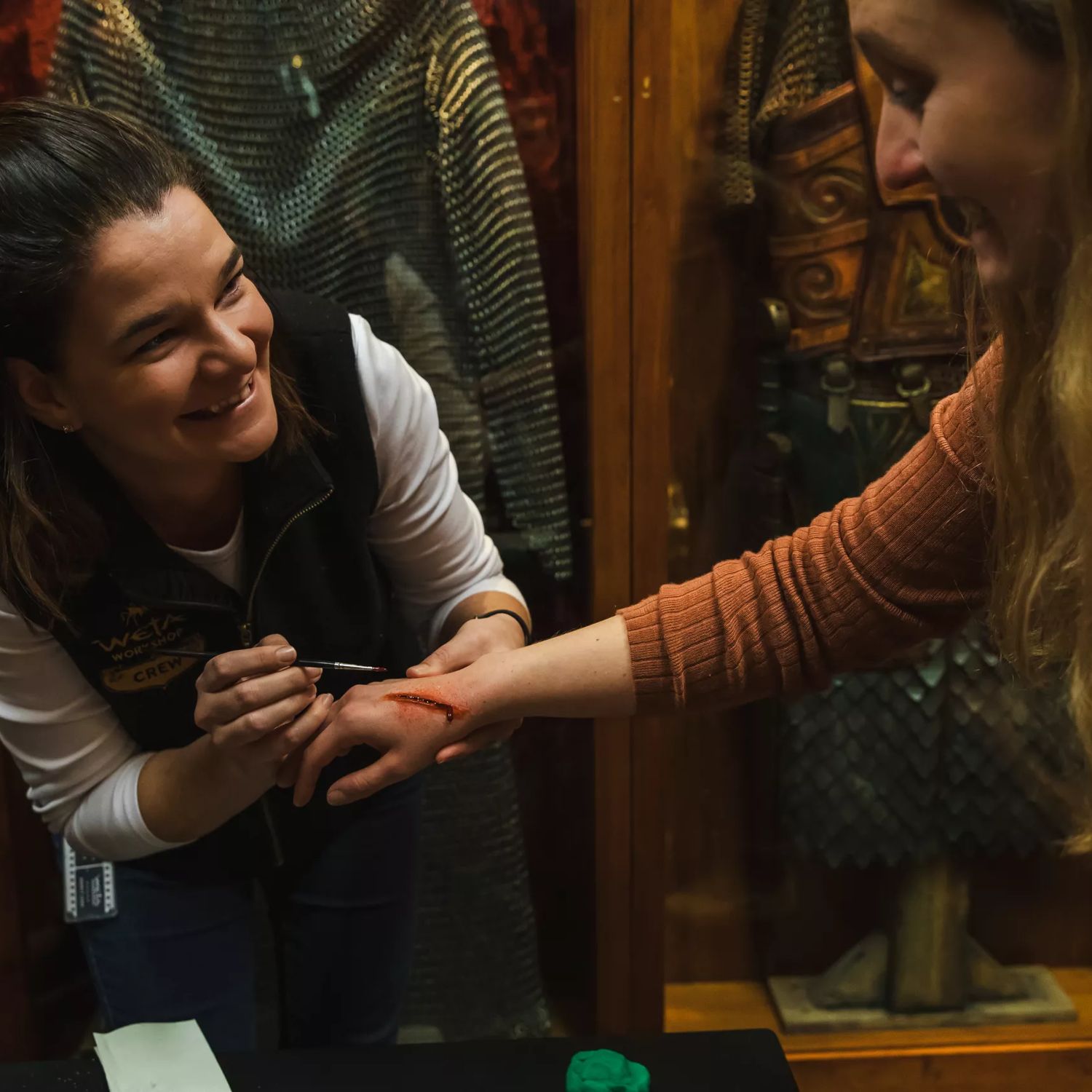 A Wētā Workshop artist applies special effects makeup to a visitor's hand, creating a realistic wound.