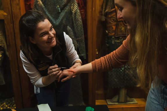 A Wētā Workshop artist applies special effects makeup to a visitor's hand, creating a realistic wound.