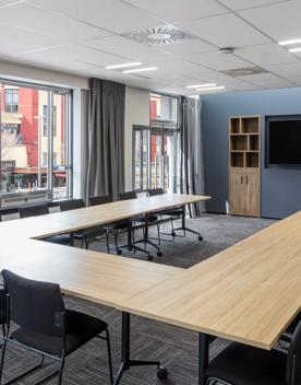 A conference room inside Oaks Wellington hotel, 16 chairs around 3 tables face toward a tv.