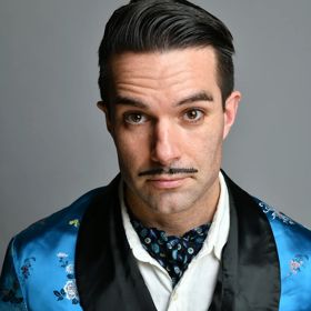 Troy Hawke smirks at the camera, wearing a blue silk robe.