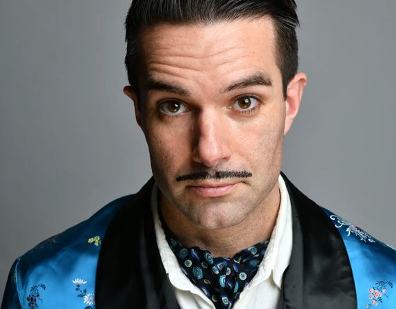 Troy Hawke smirks at the camera, wearing a blue silk robe.