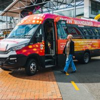 A person walking toward a colourful minibus, covered with World of WearableArt branding and text.