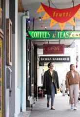 2 people walking down Cuba street underneath signs overhead.