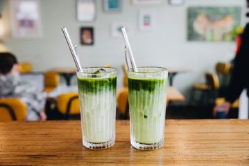 Two iced matcha in glasses with straws.
