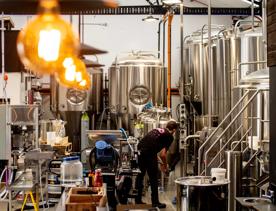 Inside Double Vision Brewing, a worker wearing all black is surrounded by many large silver tanks.