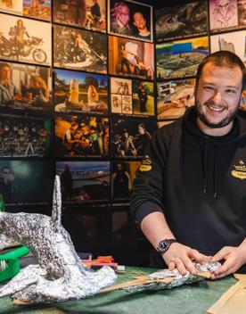 A smiling worker at Wētā Cave wears a black hoodie and works on a model using cardboard and aluminium foil.