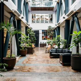 The Atrium space at The Exchange has wooden floors, steel beams, large planter boxes, sofas, and a high ceiling.