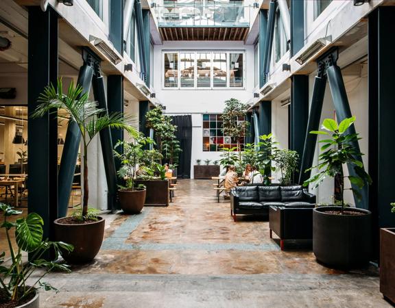The Atrium space at The Exchange has wooden floors, steel beams, large planter boxes, sofas, and a high ceiling.