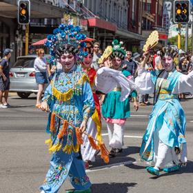 Five dancers dressed in traditional Chinese garments walk along the street.