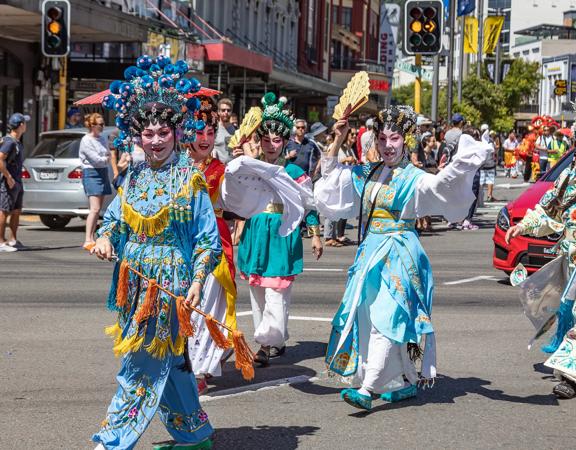 Five dancers dressed in traditional Chinese garments walk along the street.