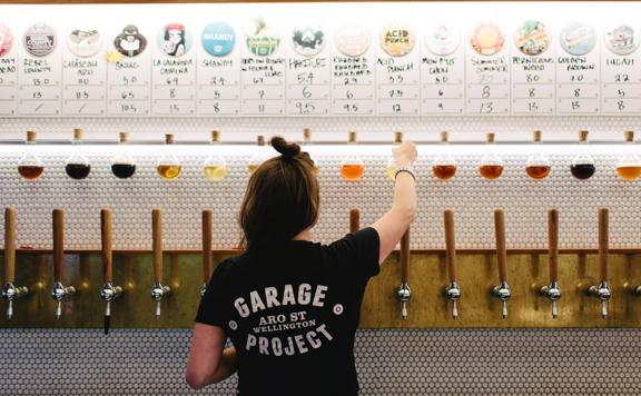At the Garage Project Taproom, numerous beer tabs line the tiled wall as a server in a Garage Project t-shirt pulls a tap.