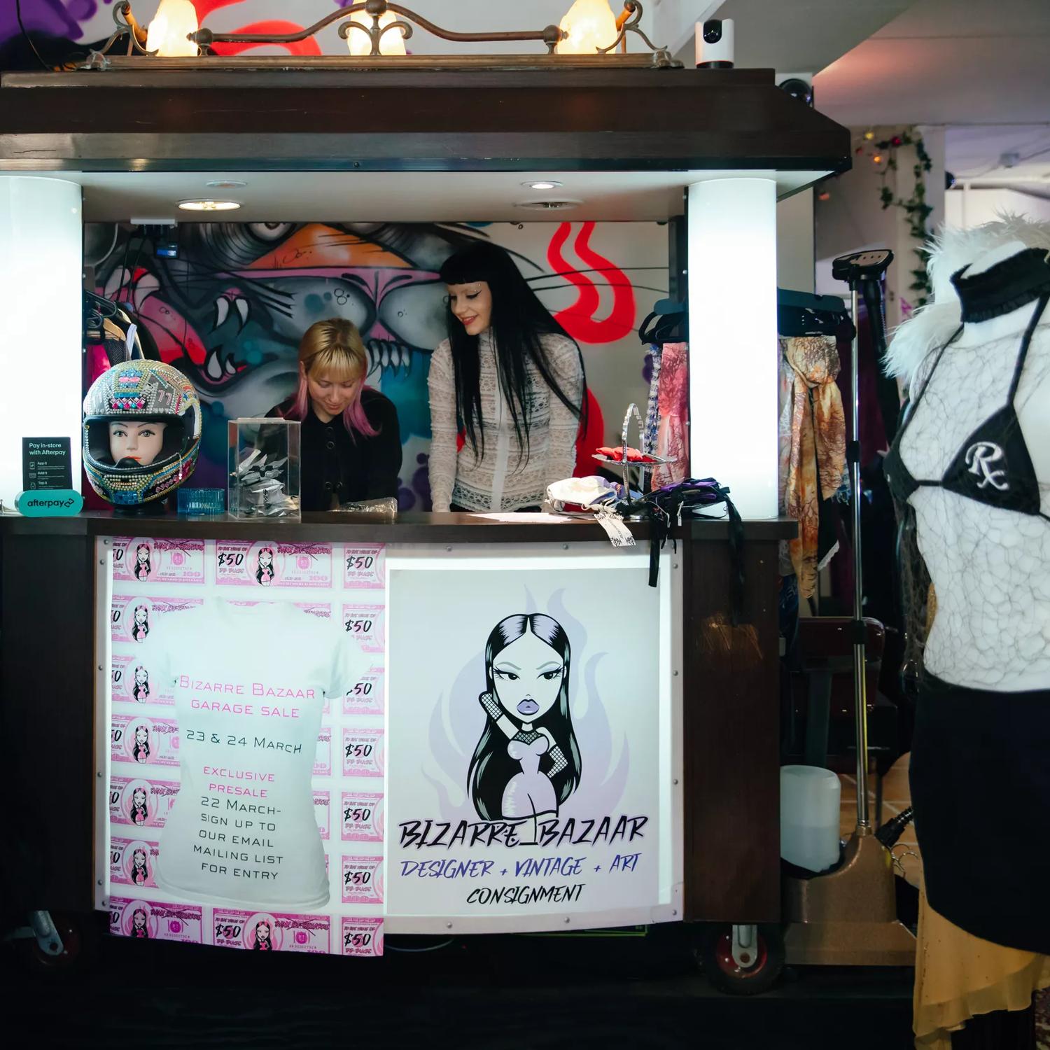 Two employees are behind the counter at Bizarre Bazaar, a secondhand clothing store in Wellington.