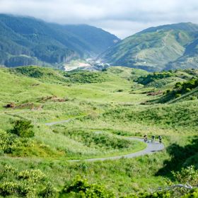A wide shot of three cyclists on a winding path in a grassy valley in Queen Elizabeth Park.