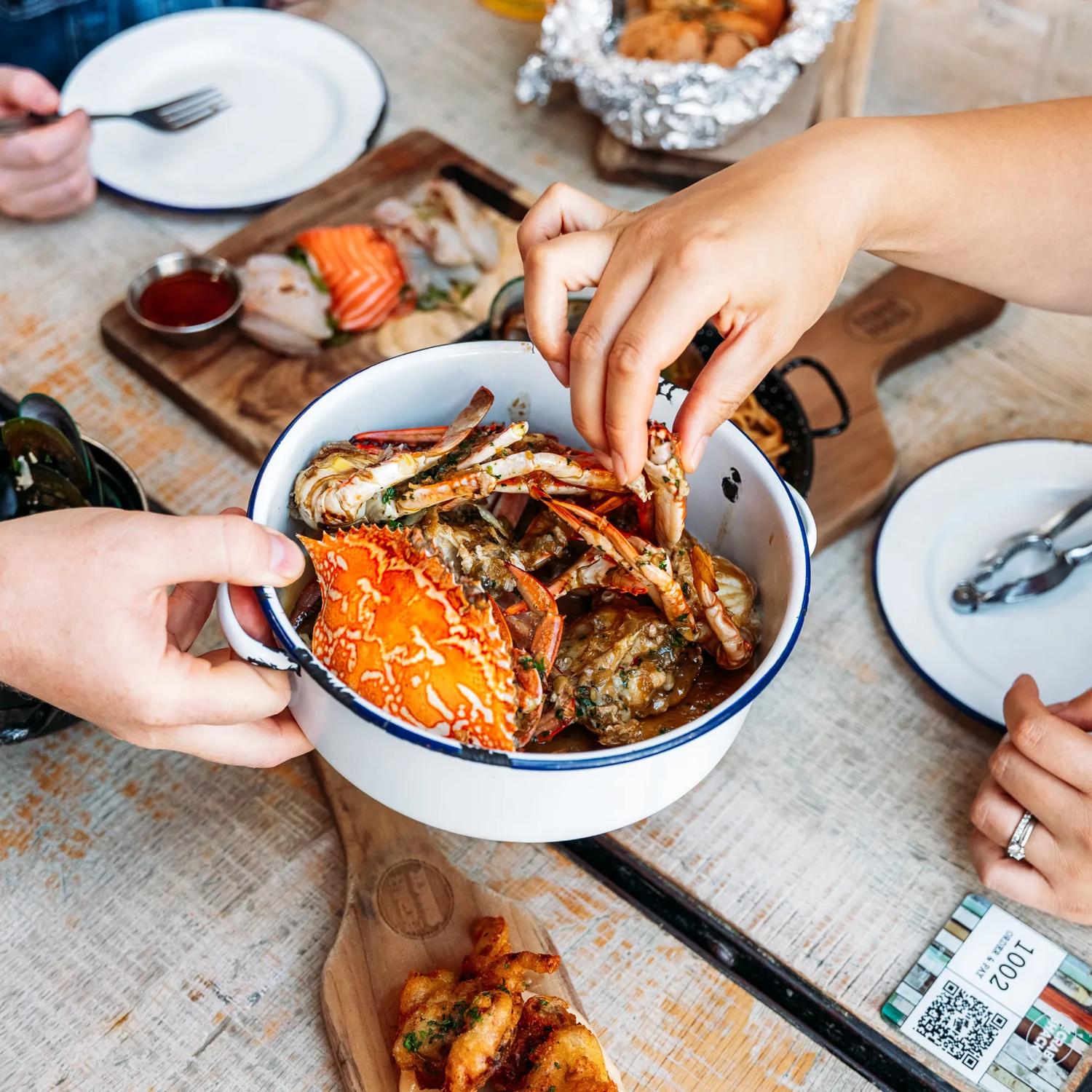 Three people eat crab and other seafood plates at The Crab Shack on Queens Wharf.