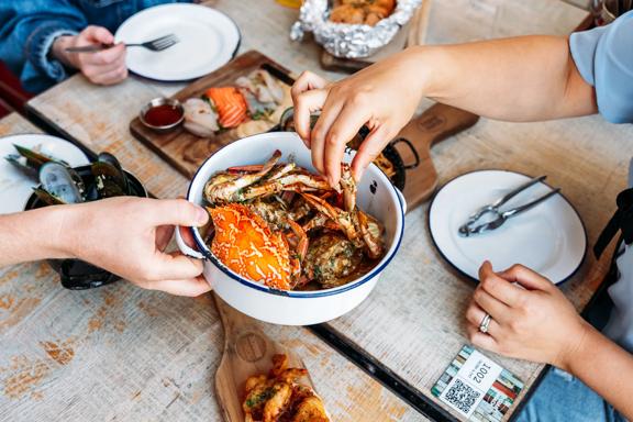 Three people eat crab and other seafood plates at The Crab Shack on Queens Wharf.