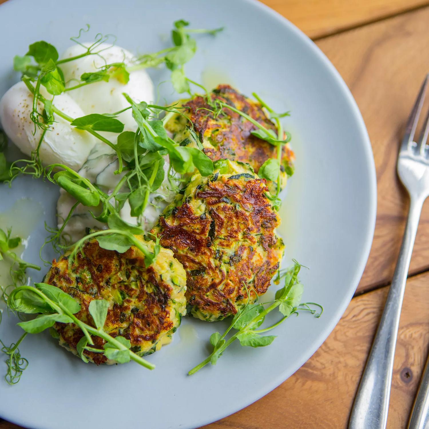 A plate of three plant-based fritters, garnished with micro-greens with a fork and knife next to it on a table at The Botanist, a restaurant in Lyall Bay, Wellington. 