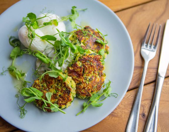 A plate of three plant-based fritters, garnished with micro-greens with a fork and knife next to it on a table at The Botanist, a restaurant in Lyall Bay, Wellington.