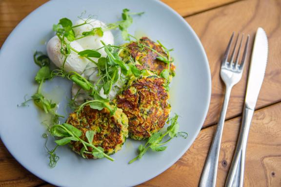 A plate of three plant-based fritters, garnished with micro-greens with a fork and knife next to it on a table at The Botanist, a restaurant in Lyall Bay, Wellington.