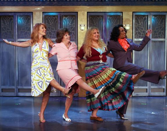 Four joyful actresses line up on stage, kicking their right legs high in a spirited can-can routine.