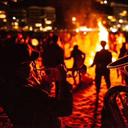 Brass musicians perform at a bonfire on the beach.