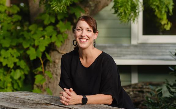 Gillian Boucher, founder Orba Shoes, sits at a picnic table. She wears a black top and is smiling. 