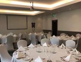 4 tables in a business room inside Copthorne hotel, with white table cloths, White napkins, white chairs and plates with utensils