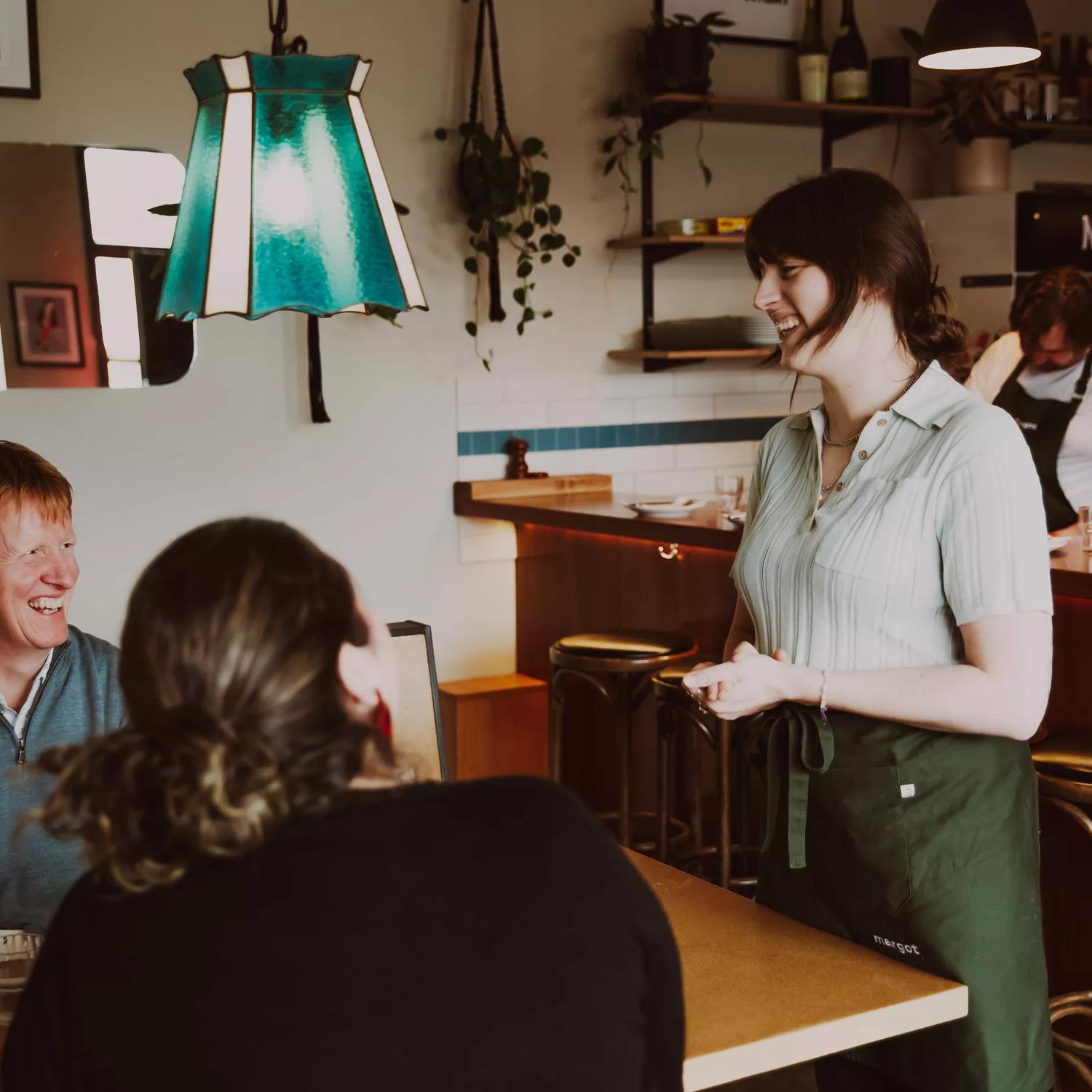 Two people are seated while a server stands by the table at Margot, a bar and restaurant located in Newtown, Wellington. 