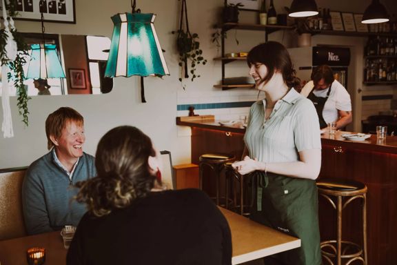 Two people are seated while a server stands by the table at Margot, a bar and restaurant located in Newtown, Wellington.